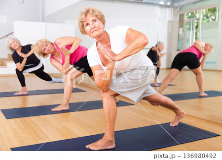 Group aged women standing in yoga pose indoors Group aged women standing in yoga pose indoors 136980492