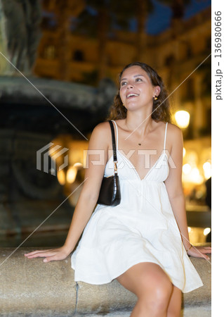young woman sitting near a fountain in the evening 136980666