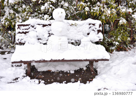公園のベンチに降る雪と雪だるま 136980777