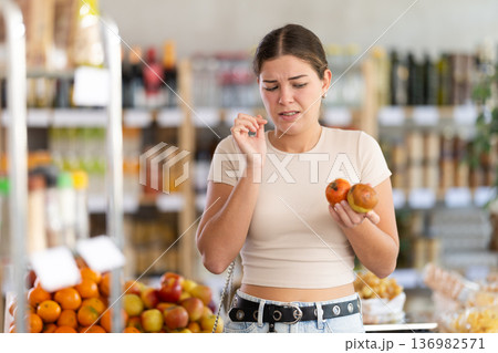 In store, frustrated girl holds rotten fruits in hands. 136982571
