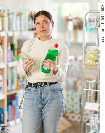 Girl housewife in household store examines package, chooses dishwashing 136982602