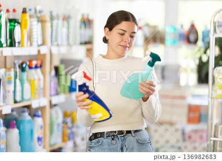 Girl housewife in household store examines package, chooses household chemical spray Girl housewife in household store examines package, chooses household chemical spray 136982683