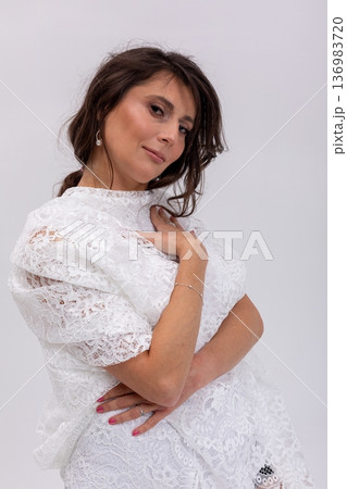 Confident woman in white dress standing with crossed arms, assertive expression and poised stance, editorial corporate aesthetic with subtle jewelry and strong presence 136983720
