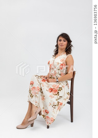 Elegant woman in relaxed pose, Stylish woman with crossed ankles and gentle smile, Professional studio shot of relaxed woman dressed in floral attire with subtle heels Elegant woman in relaxed pose, Stylish woman with crossed ankles and gentle smile, Professional studio shot of relaxed woman dressed in floral attire with subtle heels 136983756