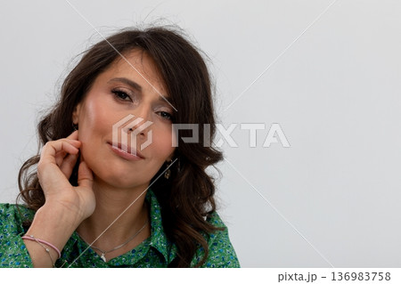 Contemplative woman refining her ear adornment elegantly, Professional studio photography capturing woman with soft hair and confident demeanor focusing on her accessory 136983758