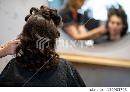 Stylist adding finishing touches to curled hair, last checks in mirror, subtle smoothing and shaping, anticipation of final look, organized station in background 136983768