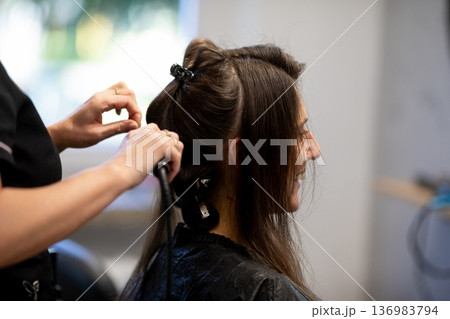 Calm atmosphere during hair styling process, Closeup of stylist working on damp hair in salon, Candid scene showing stylist carefully braiding damp hair with warm lighting Calm atmosphere during hair styling process, Closeup of stylist working on damp hair in salon, Candid scene showing stylist carefully braiding damp hair with warm lighting 136983794