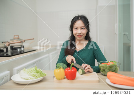 Young woman preparing fresh vegetables in a bright kitchen, practicing healthy cooking with colorful ingredients for a nutritious meal at home 136984521