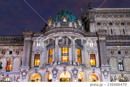 Night view of the illuminated historic architecture and ornate facade of the Palais Garnier opera house in Paris, France. Night view of the illuminated historic architecture and ornate facade of the Palais Garnier opera house in Paris, France. 136986470