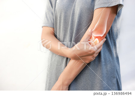 Asian woman suffering from elbow joint pain with red x-ray bone graphic overlay, female touching arm feeling ache from inflammation, arthritis, tendonitis or injury in garden, healthcare concept. 136986494