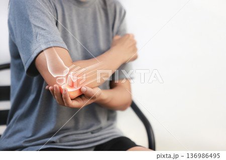 Asian woman suffering from elbow joint pain with red x-ray bone graphic overlay, female touching arm feeling ache from inflammation, arthritis, tendonitis or injury in garden, healthcare concept. 136986495