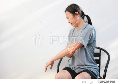 Asian woman suffering from elbow joint pain with red x-ray bone graphic overlay, female touching arm feeling ache from inflammation, arthritis, tendonitis or injury in garden, healthcare concept. 136986496