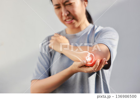 Asian woman suffering from elbow joint pain with red x-ray bone graphic overlay, female touching arm feeling ache from inflammation, arthritis, tendonitis or injury in garden, healthcare concept. Asian woman suffering from elbow joint pain with red x-ray bone graphic overlay, female touching arm feeling ache from inflammation, arthritis, tendonitis or injury in garden, healthcare concept. 136986500