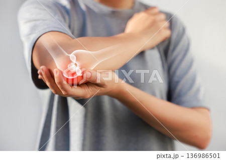 Asian woman suffering from elbow joint pain with red x-ray bone graphic overlay, female touching arm feeling ache from inflammation, arthritis, tendonitis or injury in garden, healthcare concept. 136986501