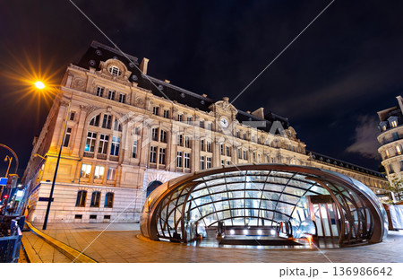 Night view of a modern glass dome metro entrance in front of the illuminated historic Gare Saint Lazare train station building in Paris, France. Night view of a modern glass dome metro entrance in front of the illuminated historic Gare Saint Lazare train station building in Paris, France. 136986642