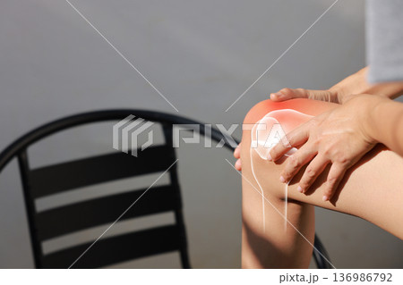 Asian woman sitting on stairs suffering from knee pain with red x-ray bone graphic overlay, female touching leg feeling ache from osteoarthritis, meniscus injury or joint inflammation concept. 136986792