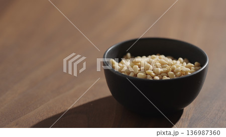 Pine nuts in a black bowl on wood table closeup Pine nuts in a black bowl on wood table closeup 136987360