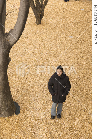 ウッドチップが敷き詰められた公園に立つ冬服の女性 ウッドチップが敷き詰められた公園に立つ冬服の女性 136987944