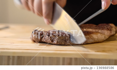The close up image of a chef cutting medium rare grilled beef steak with chef knives on a wooden chopping board. The close up image of a chef cutting medium rare grilled beef steak with chef knives on a wooden chopping board. 136988586