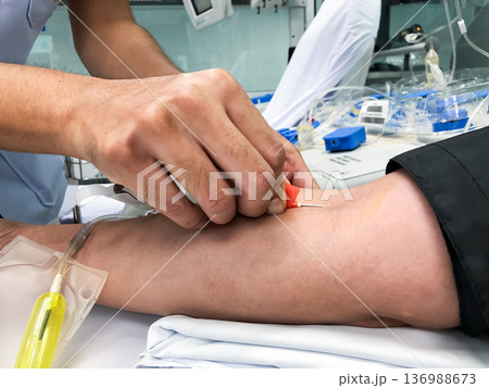 Blood platelet donation, a male nurse inserts a needle into donor arm to draw blood at a hospital. 136988673