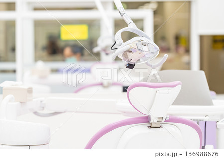 The side view of a modern white dental light lamp and reflector equipment above a medical chair on a blurry background of a dental clinic. 136988676