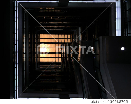 Stair in the square building from 1st floor shoots up to rooftop glass with the orange sunlight down on it. Stair in the square building from 1st floor shoots up to rooftop glass with the orange sunlight down on it. 136988706