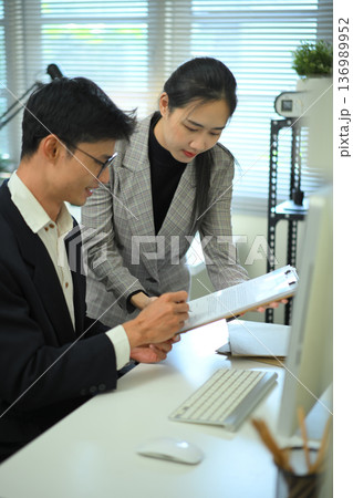 Close-up of coworkers discussing work at a desktop computer 136989952