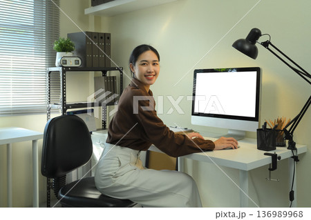 Office woman looking at camera and using blank screen computer monitor 136989968