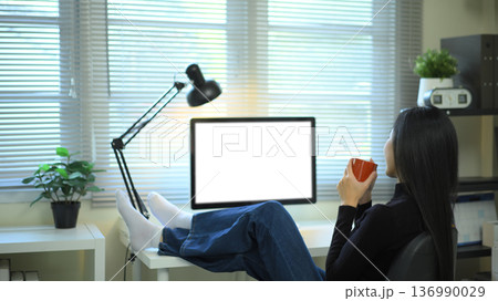 Woman relaxing with coffee at desk and empty screen computer in modern office Woman relaxing with coffee at desk and empty screen computer in modern office 136990029