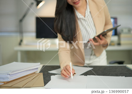 Businesswoman analyzes expenses using tablet and paper. Person in suit calculates costs, income, profit, budget Businesswoman analyzes expenses using tablet and paper. Person in suit calculates costs, income, profit, budget 136990057