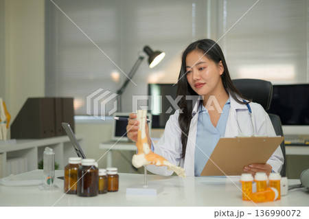 Doctor studying a bone model at a desk, showing medical learning, anatomy education, and professional training Doctor studying a bone model at a desk, showing medical learning, anatomy education, and professional training 136990072