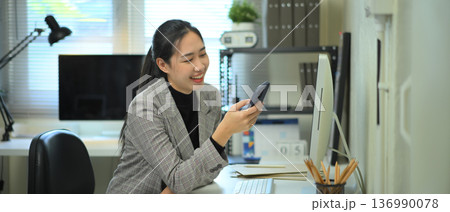 Woman using smartphone at desk in modern office workspace Woman using smartphone at desk in modern office workspace 136990078