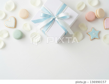 白背景に置かれた水色リボンのギフトボックスとマカロンやアイシングクッキーのフラットレイ 136990157