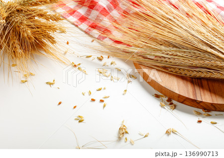 Wheat stalks and grains laying on a wooden board with a checkered cloth nearby 136990713