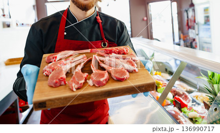 Butcher holds a wooden tray of fresh cuts of meat in a local shop during the day 136990717