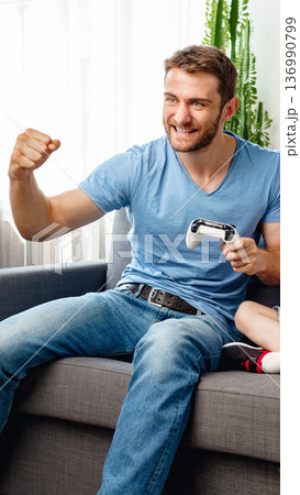 Man plays video game with child on couch during afternoon at home in living room 136990799