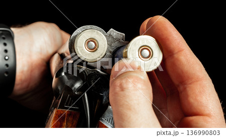 Man loading shotgun shells for shooting practice in indoor range during evening hours Man loading shotgun shells for shooting practice in indoor range during evening hours 136990803