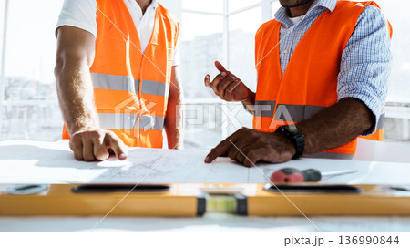 Two construction workers discuss plans in an office with bright sunlight during the day 136990844