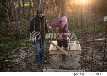 Child plays on a wooden structure with adult during sunset in a park 136990998