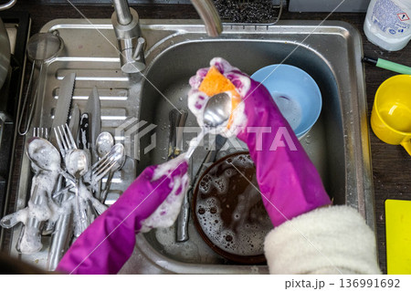 Washing dishes in kitchen sink with purple rubber gloves 136991692