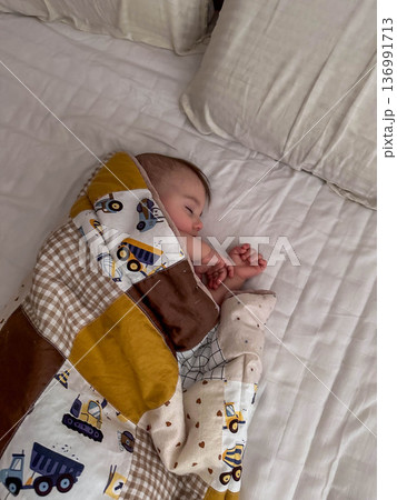 Peaceful sleeping baby under patchwork quilt on white bed Peaceful sleeping baby under patchwork quilt on white bed 136991713