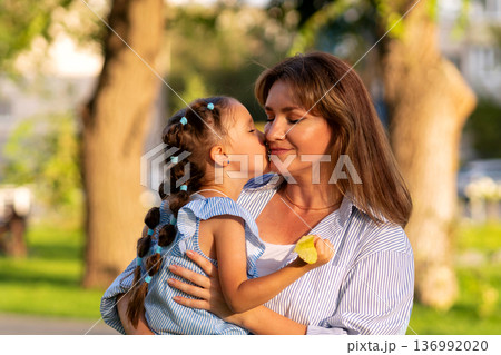 Girl kisses mom's cheek in warm sunset glow 136992020