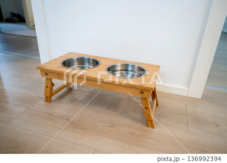 Wooden elevated pet feeder with metal bowls in minimalist Scandinavian interior 136992394