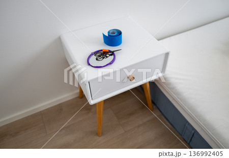 Minimalist bedside table with scissors earplugs mirror and kinesiology tape in bedroom interior 136992405