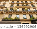 Paris classic haussmann building facade with ornate balconies, green plants, awnings, and large windows 136992906