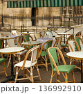 Paris street cafe terrace featuring empty bistro tables and classic wicker chairs under a green awning, awaiting customers 136992910