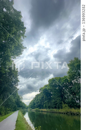 Tranquil pathway alongside reflective water beneath cloudy sky 136993282