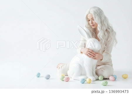 Serene Woman with Long White Hair Holding Glossy Ceramic Bunny Sculpture Surrounded by Speckled Pastel Easter Eggs Serene Woman with Long White Hair Holding Glossy Ceramic Bunny Sculpture Surrounded by Speckled Pastel Easter Eggs 136993473
