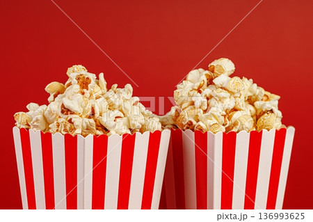 Delicious popcorn in two paper cups on red background. Home cinema and party snack. Delicious popcorn in two paper cups on red background. Home cinema and party snack. 136993625