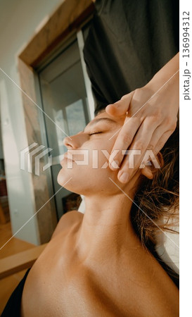Serene scene where woman receives calming facial massage by sunny window 136994312